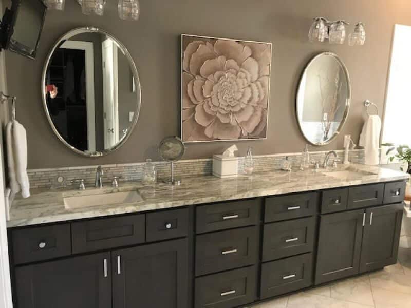 Double sink bathroom vanity with granite top, round mirrors, and floral wall art.