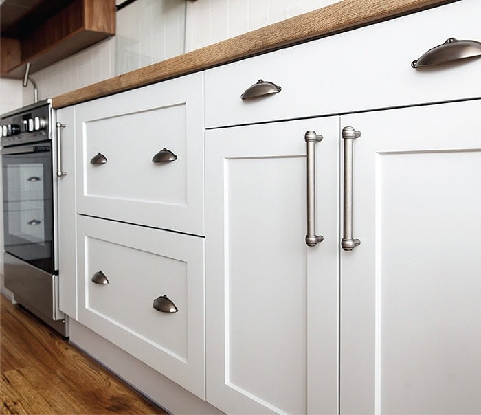 White kitchen cabinets with silver handles and wooden countertop.