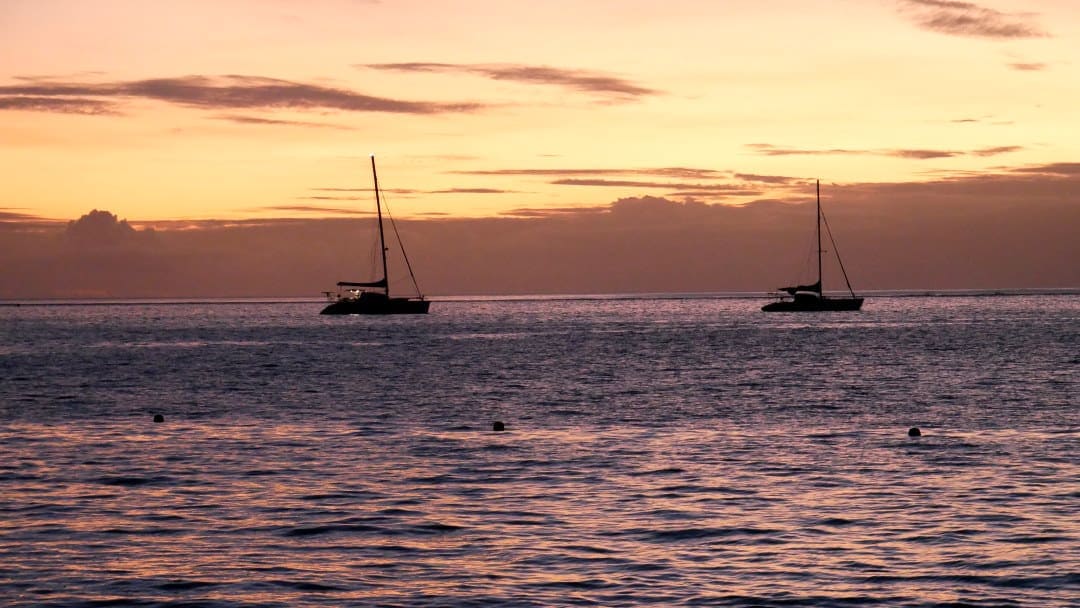 Orange sunset with two sailboats anchored in Moorea