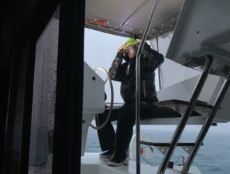Matt at the helm of Sea Odyssey with goggles on looking scared in 60 knots of wind