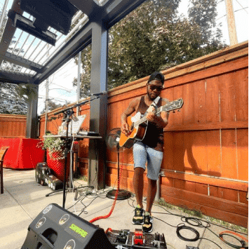 Musician playing guitar outdoors at The Holiday Bar with sound equipment.