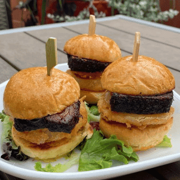 Three mini gourmet burgers with beef patties and seaweed on a white plate.