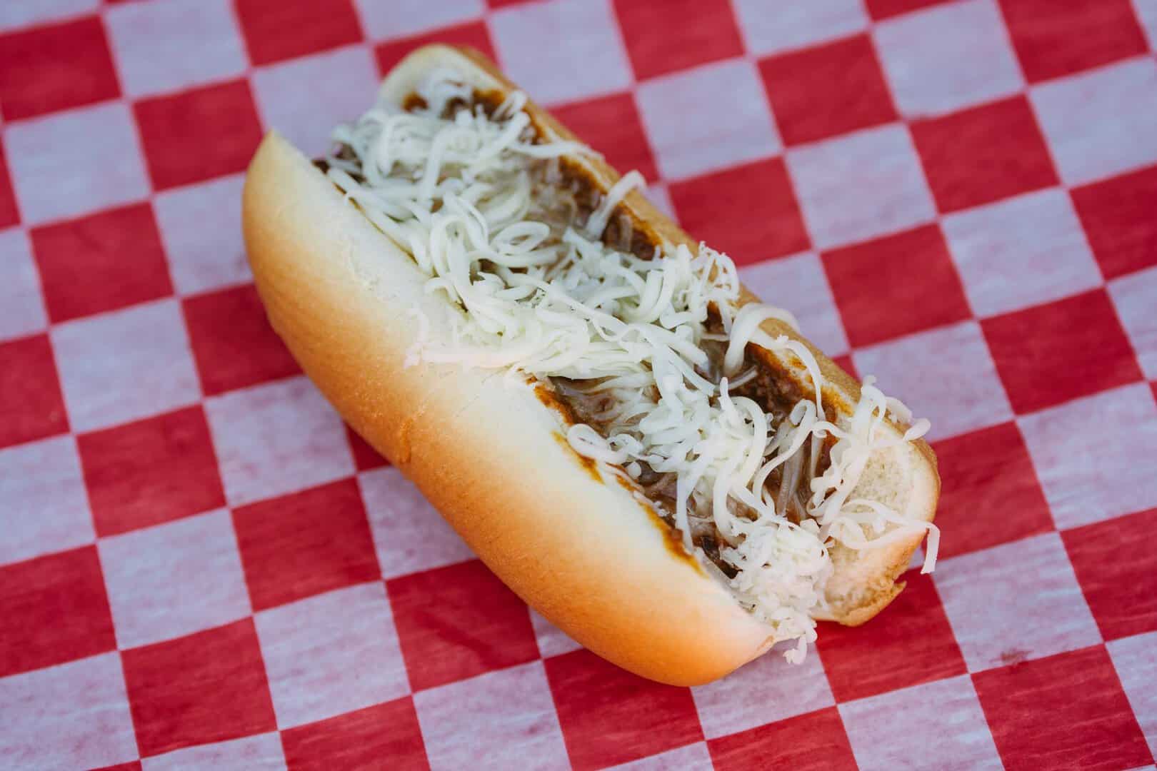 Hot dog with shredded cheese in a bun on red checkered paper.