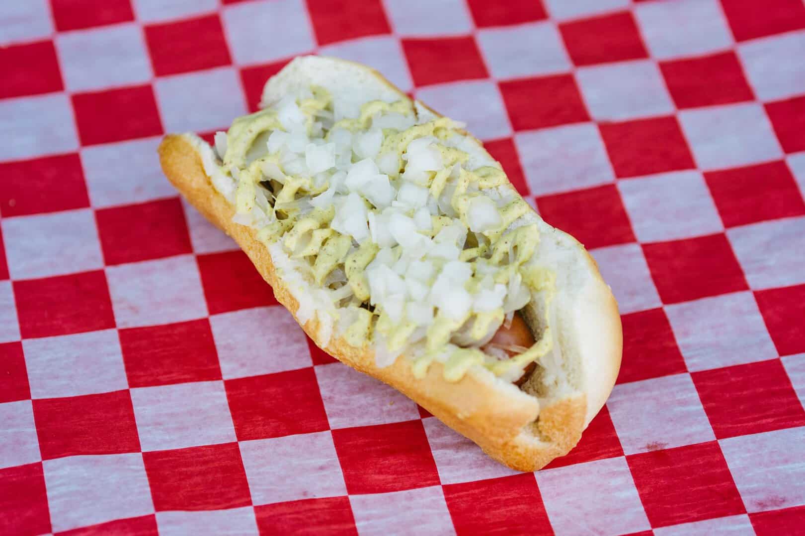 Close-up of a hot dog with onions and relish on a checkered tablecloth.