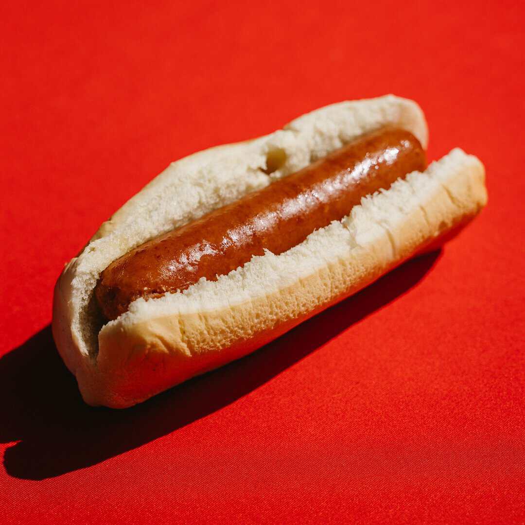 Hot dog in a bun with sausage on a red background.