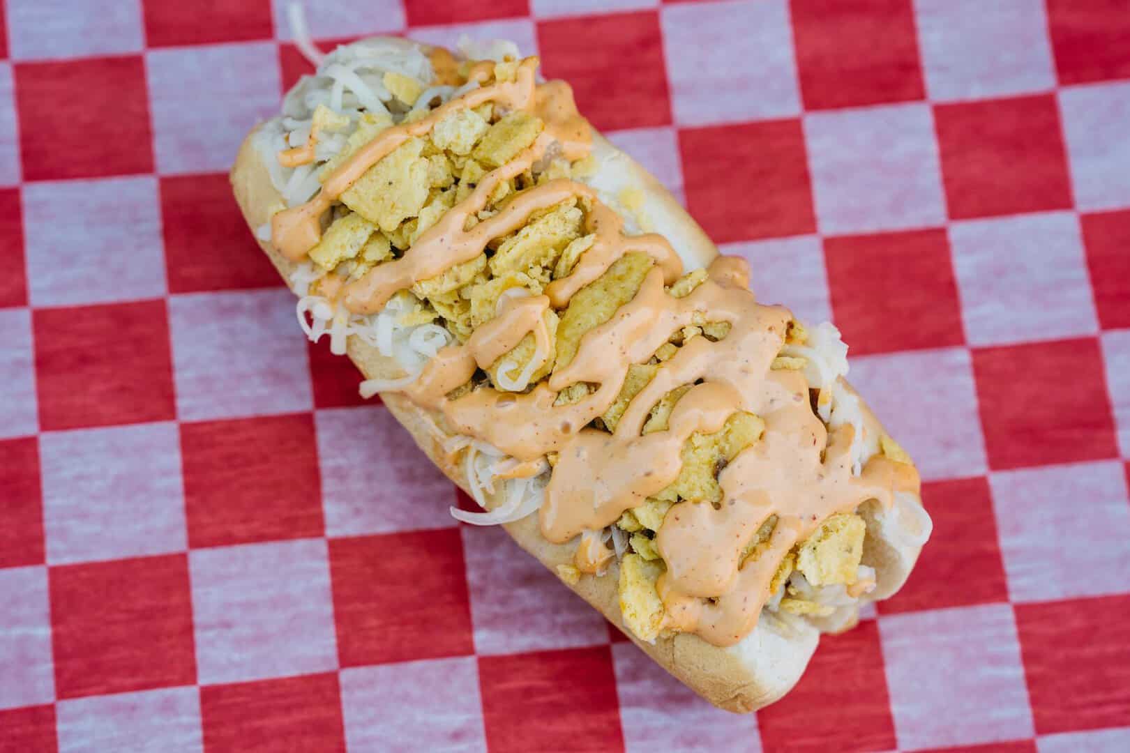 Hot dog with toppings on a checkered paper at a food stand.