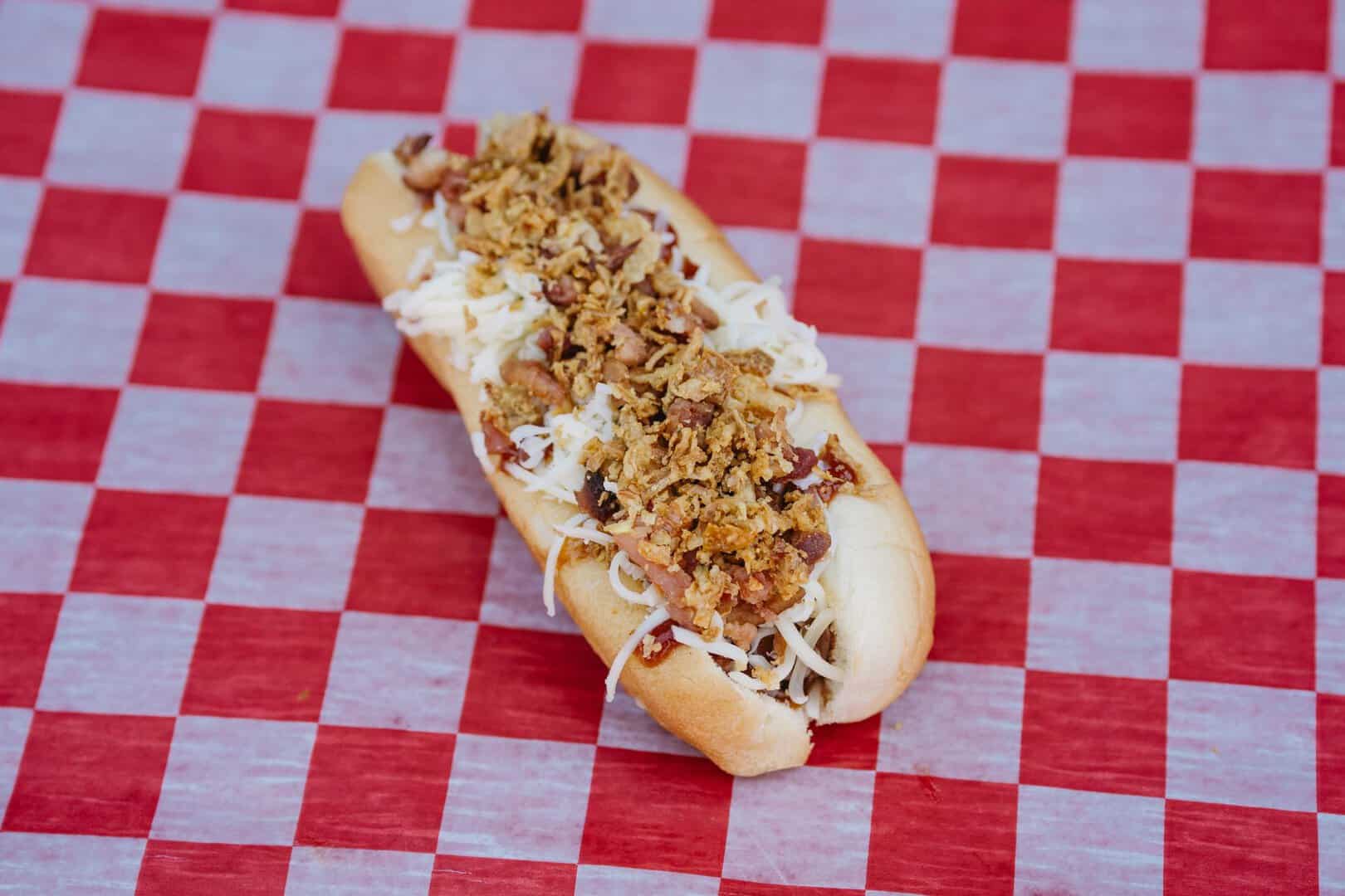 Delicious hot dog with crispy fried onions and shredded cheese on a bun.