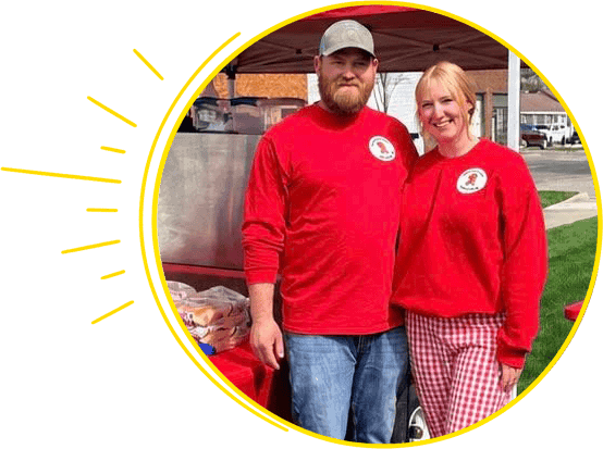 Two team members in red shirts at community event, smiling and ready to assist.