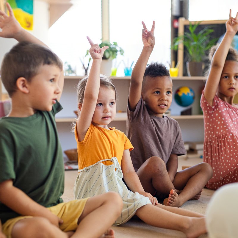 kindergarten kids raising their hands in class