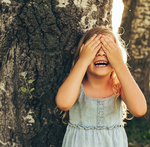 little girl playing hide and seak behind a tree