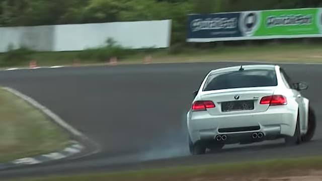 En hvid bil drifter rundt i et sving på en racerbane.