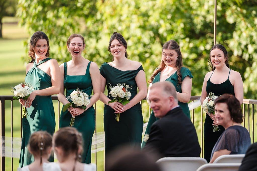 Bridesmaids react with laughter as the flower girls walk down the aisle during Bridget and Matt’s wedding ceremony at Bartlett Hills Golf Club in Bartlett, IL
