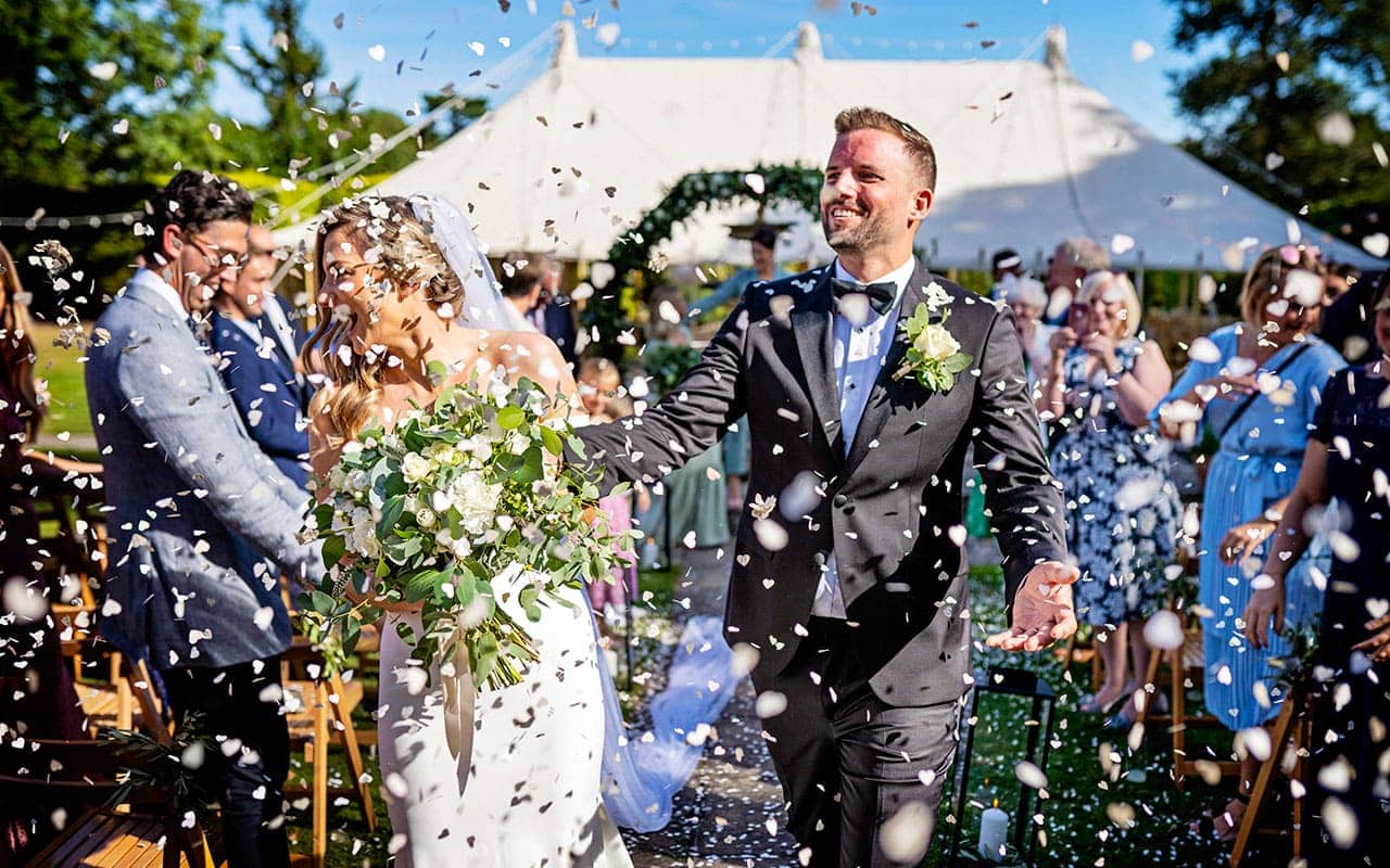 Couple leaving their marquee wedding in a cloud of confetti