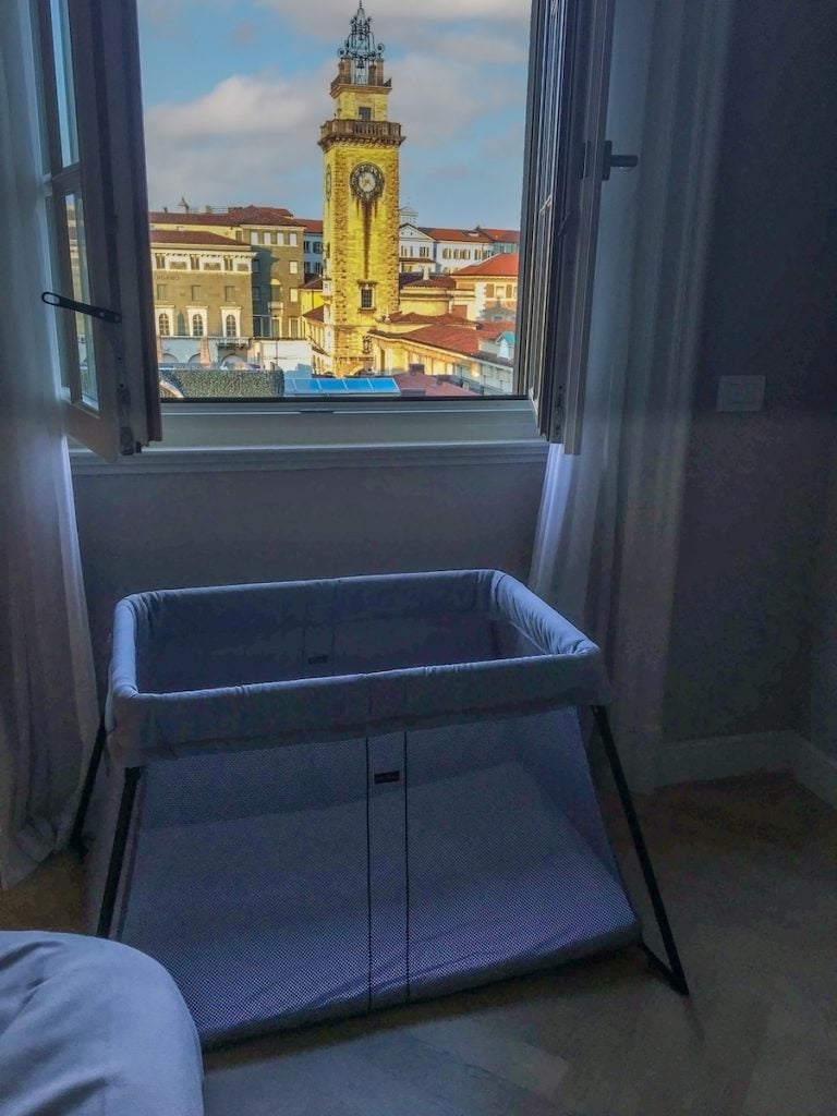 BabyBjorn Travel Crib Light Review. The Baby Bjorn travel crib light sits in a hotel room near the window. A beautiful view of Bergamo, Italy is out the window.