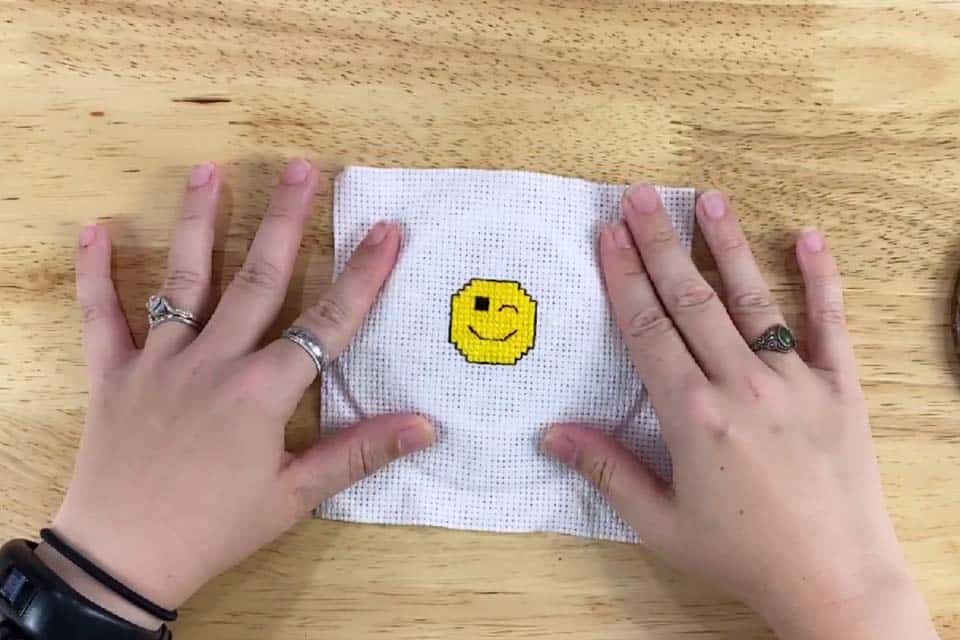 Two hands, open and pushing down on embroidery fabric so that a round shape can be seen from an embroidery hoop underneath.