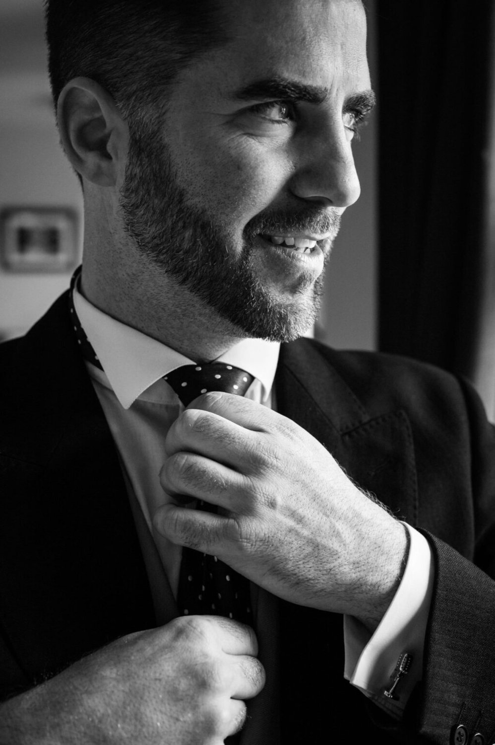 The Groom adjusts his tie by the window