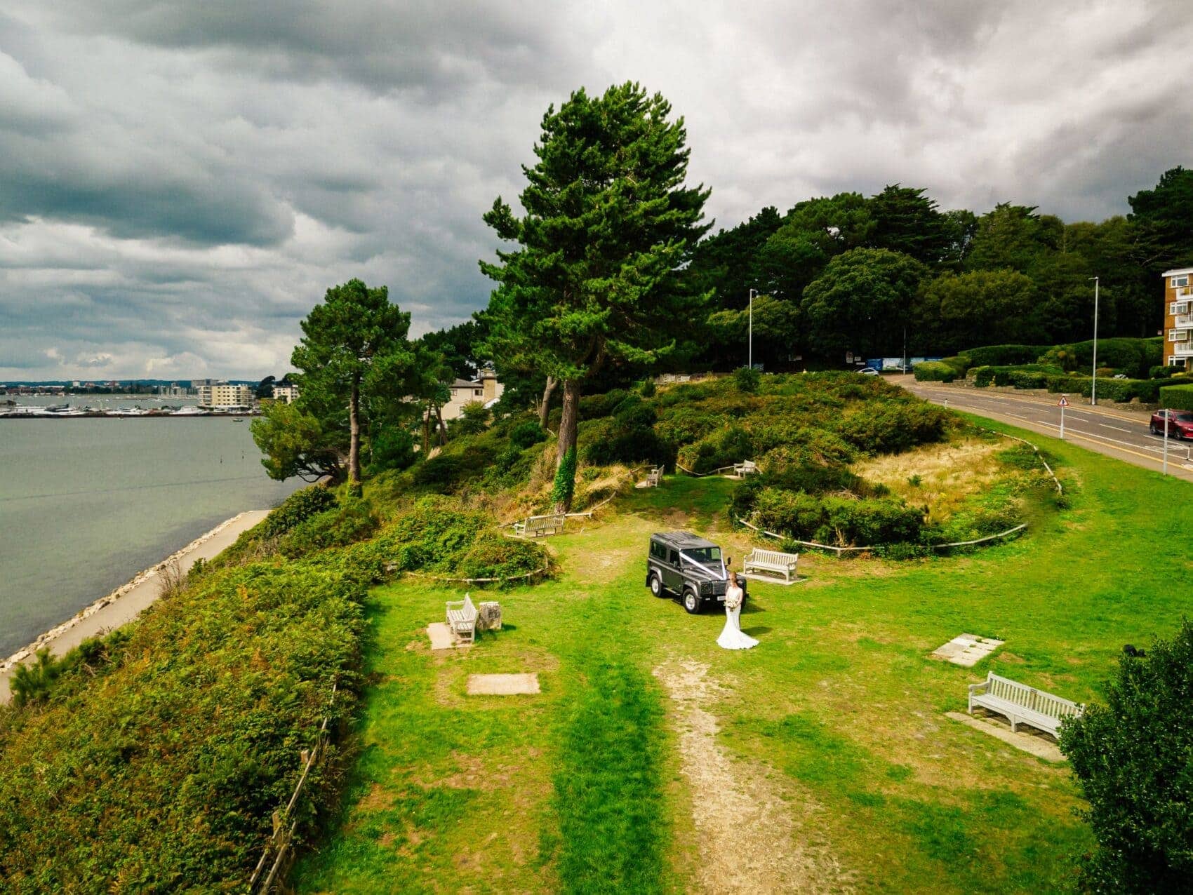 Bride and Groom with Land Rover Defender from the air at evening hill, Poole harbour