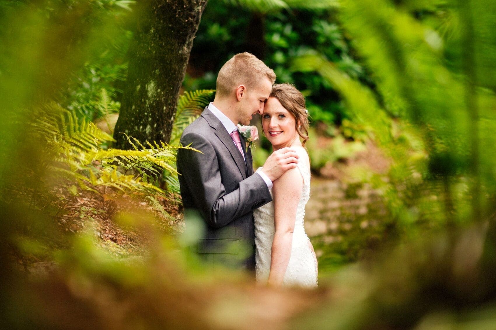 Bride looks directly at camera while hugged by the groom at Compton Acres in Poole