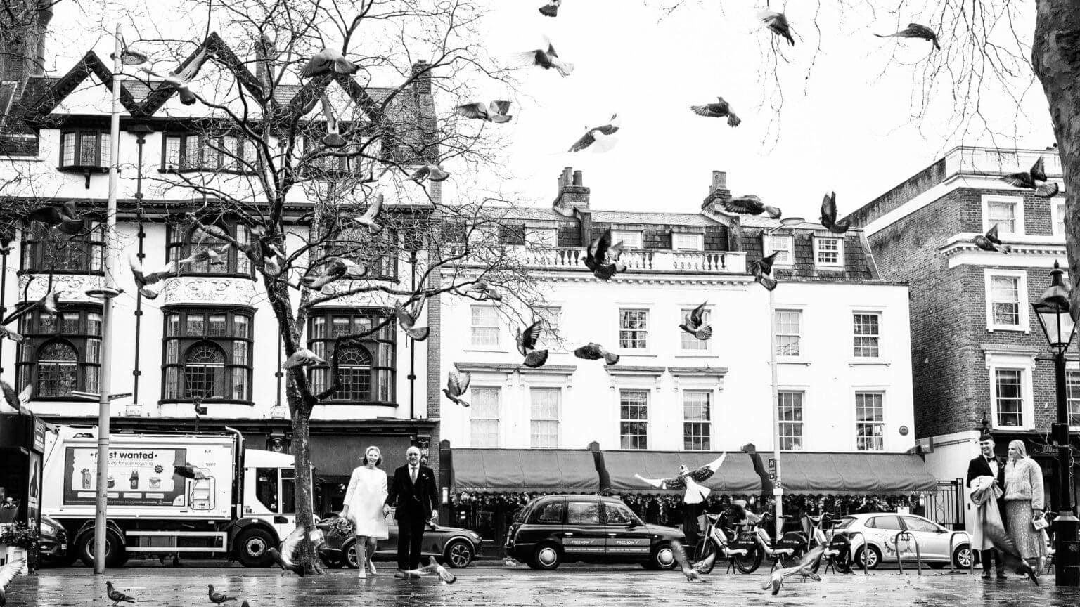 Bride and Groom walk with pidgeons flying above outside the Ivy restaraunt in London