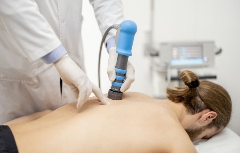 Ein Arzt behandelt den Rücken eines Patienten mit einem fokussierten Stoßwellengerät in einer Praxis.