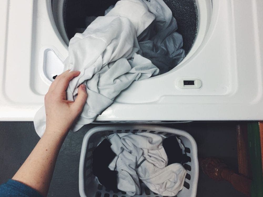 person taking clothes out of laundry machine into basket