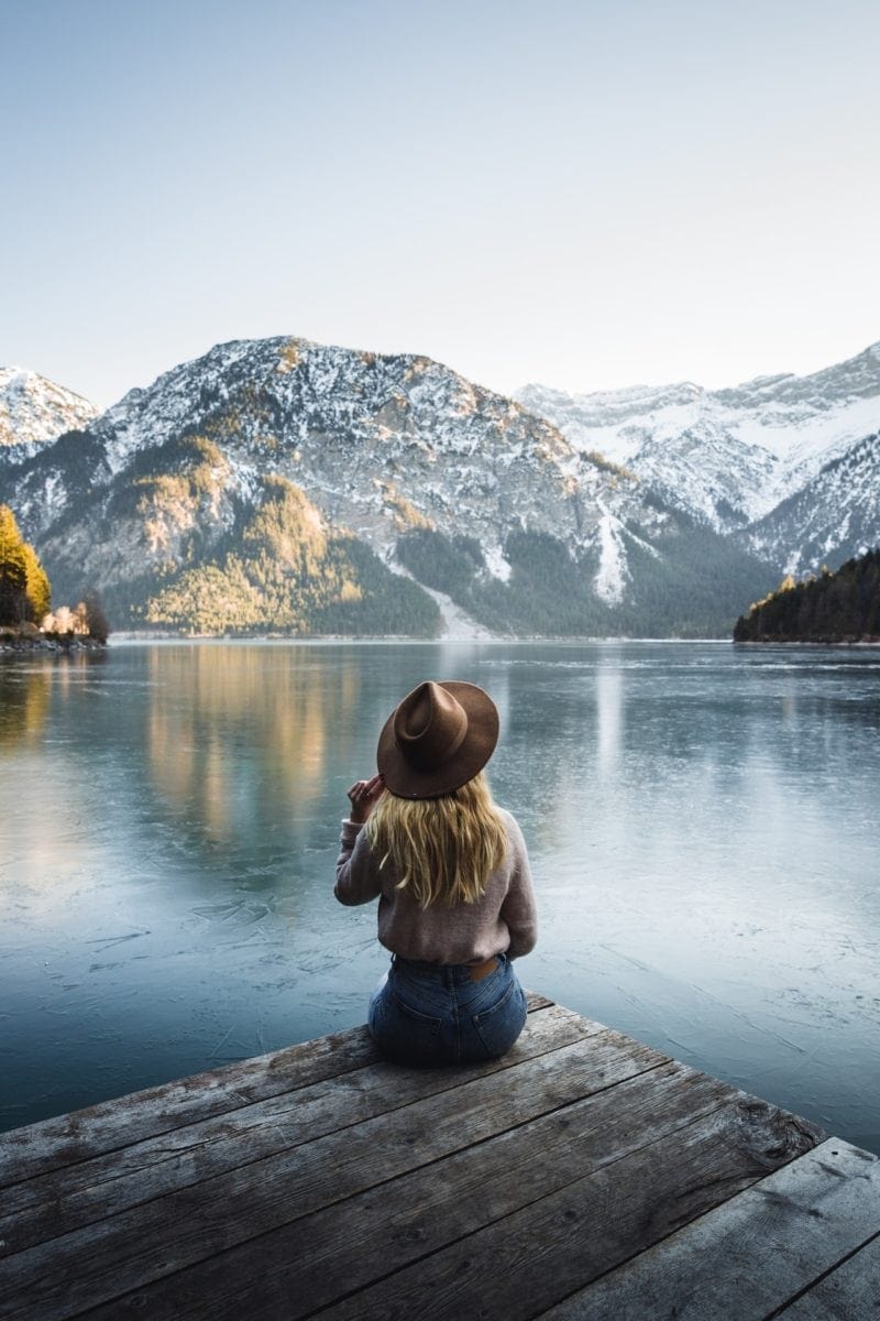 woman sitting on deck in front of lake with mountains