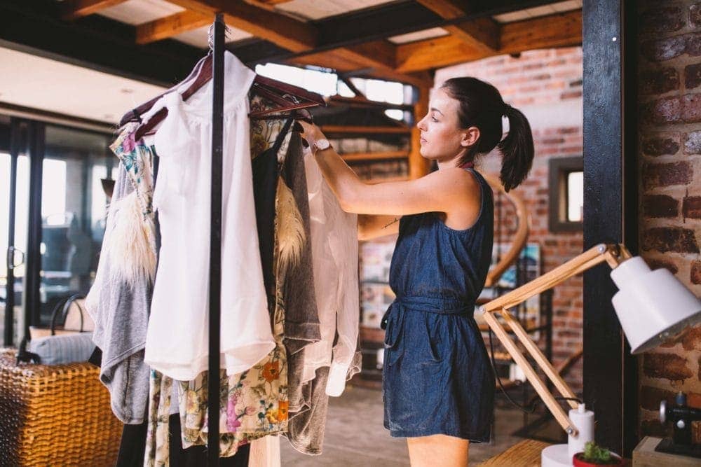 woman looking through secondhand clothing rack in thrift store