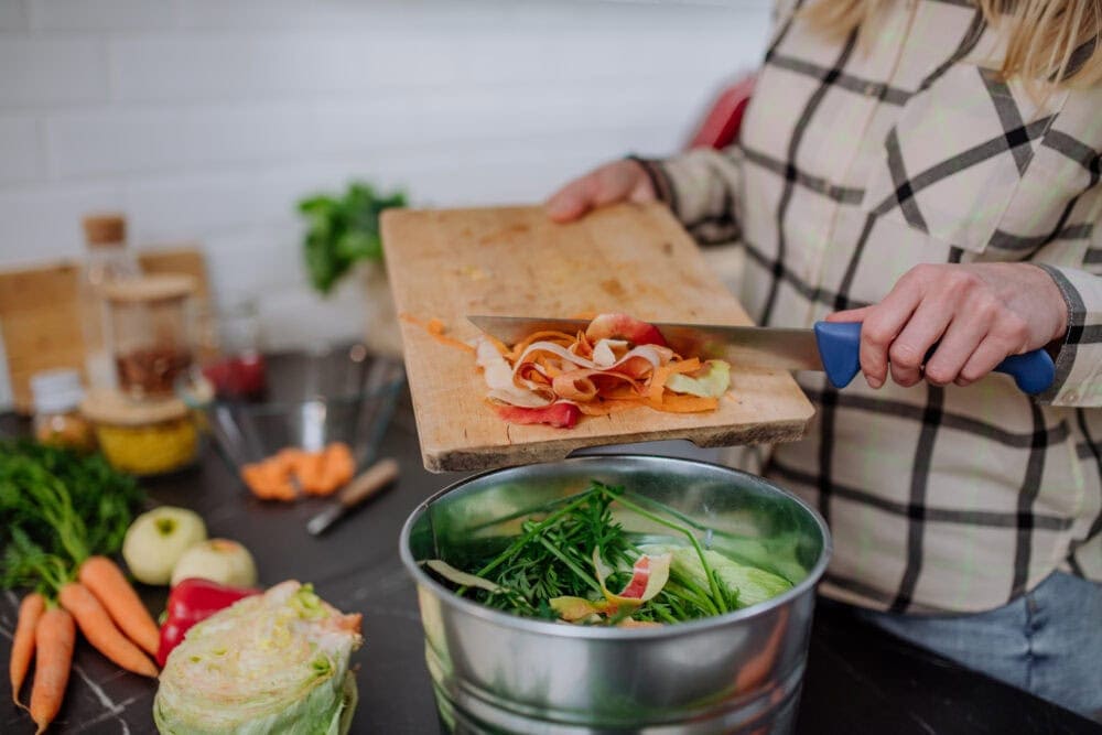 woman putting vegetable cuttings in a compost bucket