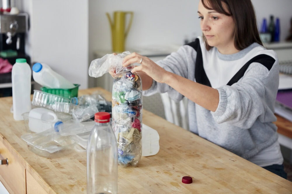 woman pushing small plastics into a plastic bottles creating an eco-brick 