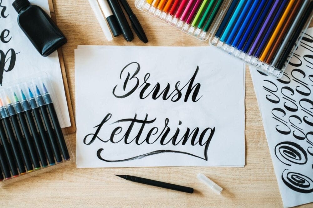 Brush Lettering text on paper and brushes and colored pencils on the table. 