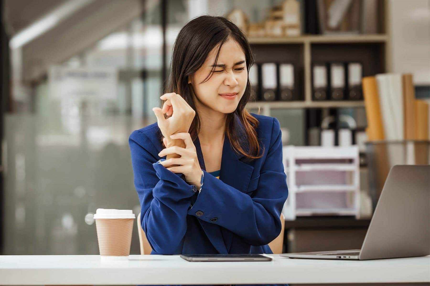 tendonitis woman holding wrist at desk
