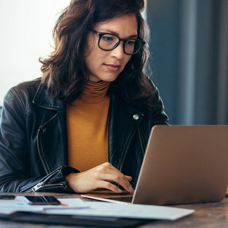 Picture of woman sat at her desk reading from the screen of her laptop. LGBCE mandatory read app case study