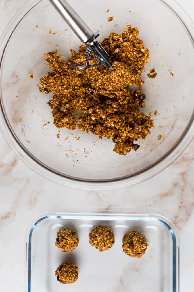 Wet and dry ingredients for no bake pumpkin energy bites combined in a mixing bowl and glass meal prep container with energy bites 