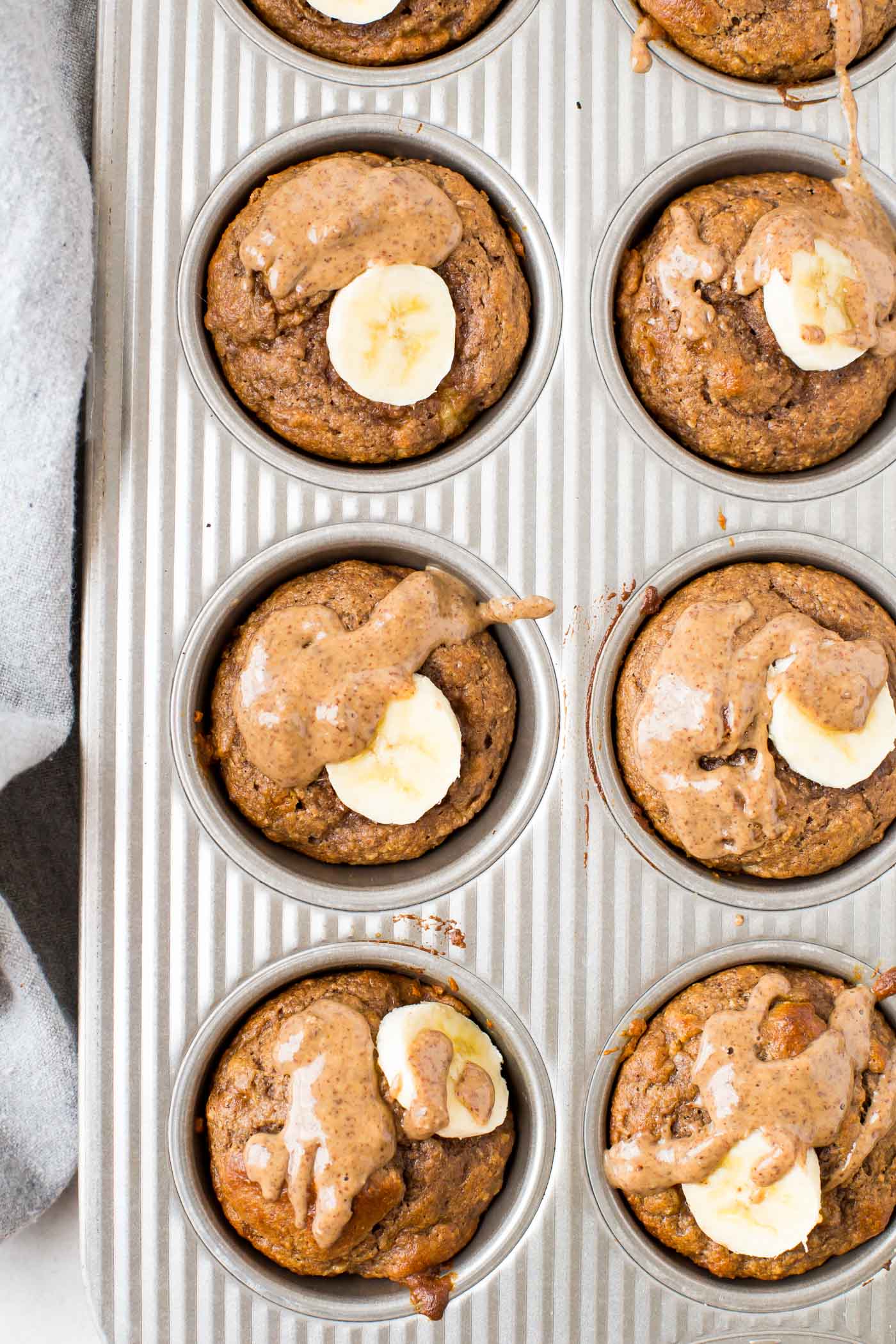 Banana Protein Muffins drizzled with almond butter in muffin tin pan