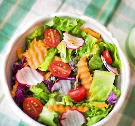 pexels-jill-wellington-1638660-257816 A bowl of fresh salad, perfect for any veganiac, features crisp lettuce, cherry tomatoes, radish slices, and crinkle-cut carrots, all set on a green checkered tablecloth.