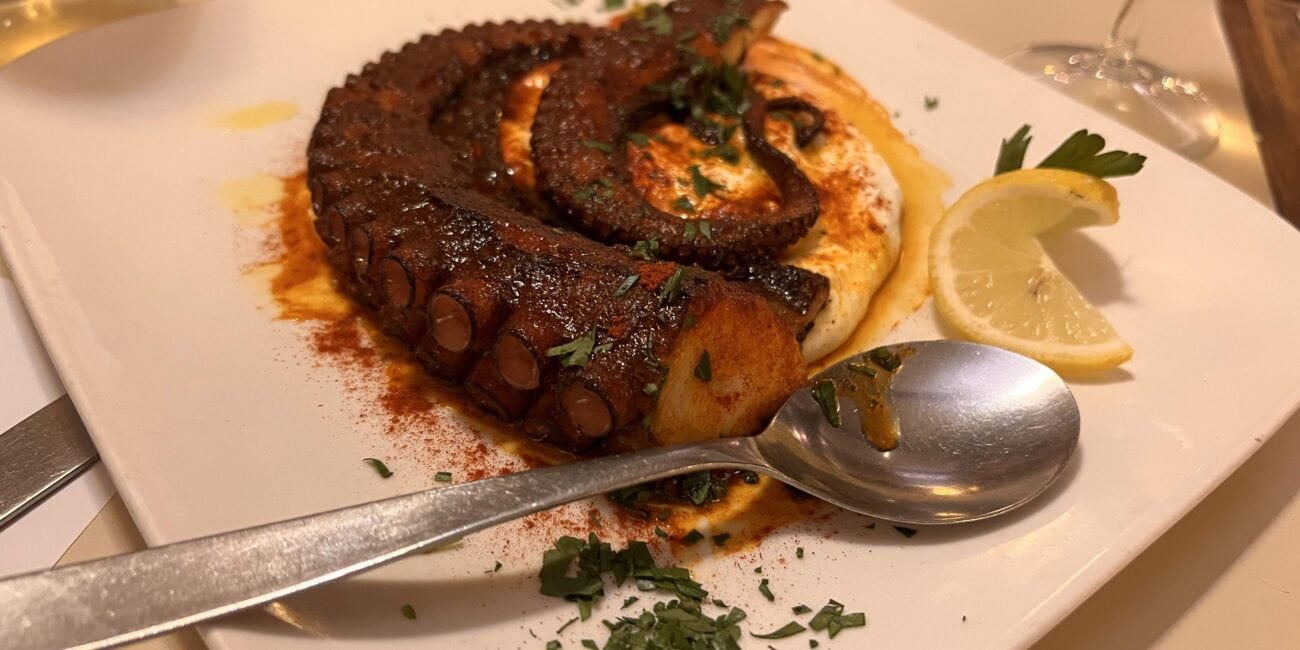 Tentáculo de polvo grelhado servido em cama cremosa, guarnecido com ervas picadas e rodela de limão em um restaurante de Punta del Este.