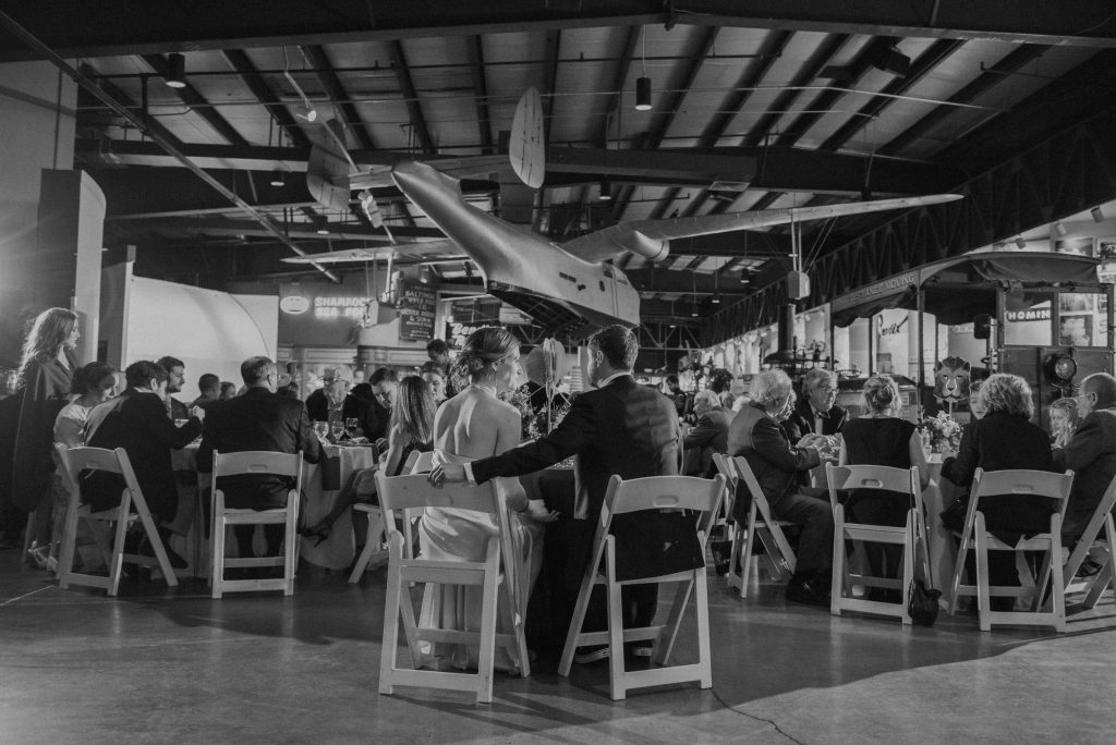A black and white view of a wedding couple with a plane hanging from the ceiling at the Baltimore Museum of Industry.