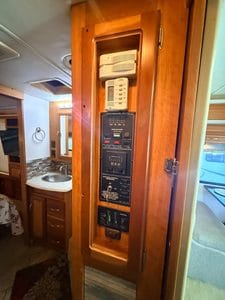 RV electrical panel with circuit breakers and switches inside a wooden cabinet.