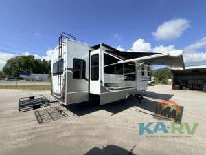 Modern RV with extended awning and outdoor stairs for camping.