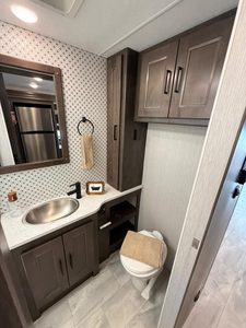 Compact RV bathroom with sink, mirror, toilet, and storage cabinets.