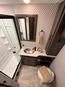 Compact RV bathroom with shower, sink, mirror, and storage for Coachmen Mirada 35OS.
