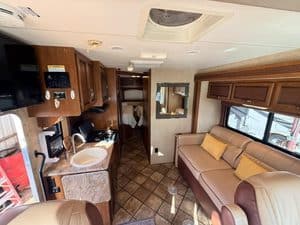 RV interior showing kitchen, sofa, and windows for travel comfort.