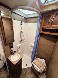 Small RV bathroom with shower, toilet, and storage cabinets.