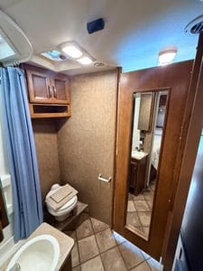 RV bathroom with wooden cabinets, mirror, and toilet in a repair setting.