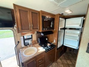 Compact RV kitchen with refrigerator, microwave, and sink for travel convenience.