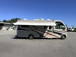 Modern RV with sleek design parked in open lot under clear blue sky.