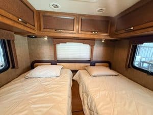 RV bedroom with two beds, wooden cabinets, and windows on both sides.