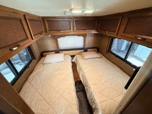 Cozy RV bedroom with two beds, windows, and wooden cabinets.