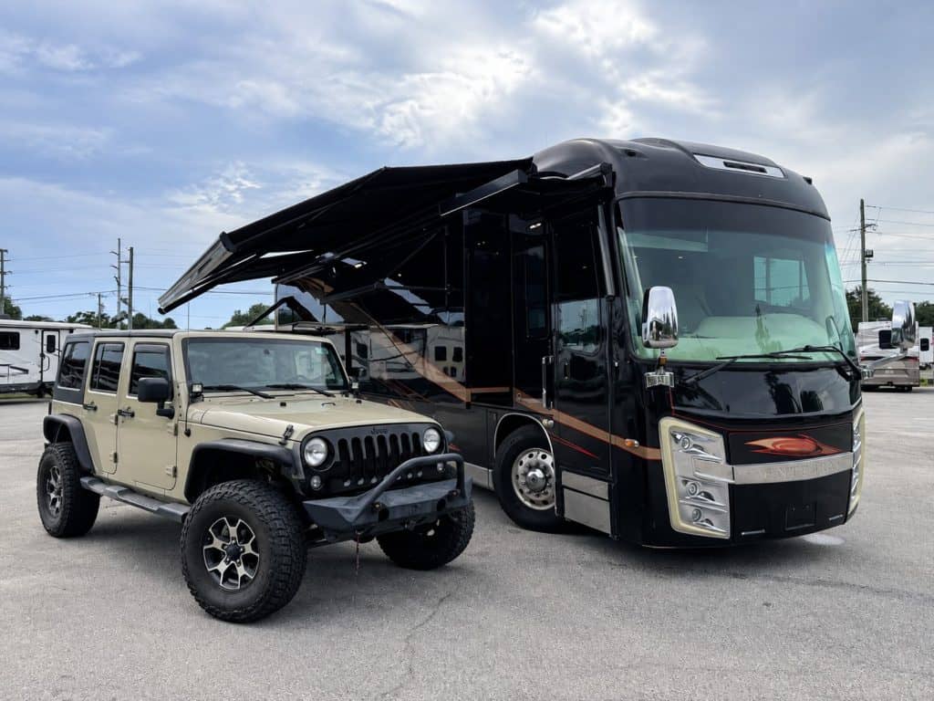 Luxury RV and rugged Jeep Wrangler parked together at dealership.