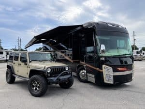 Luxury RV and rugged Jeep Wrangler parked together at dealership.